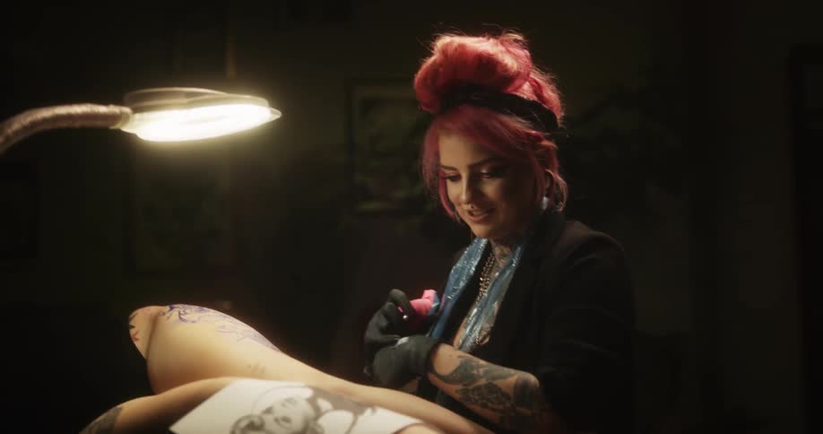 A tattoo artist looks at an art print while tattooing a man