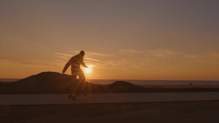Silhouette of a man riding a skateboard on a path near the beach at sunset