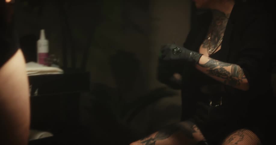 Tattoo artist wearing black latex gloves rubs gel on the leg of a client
