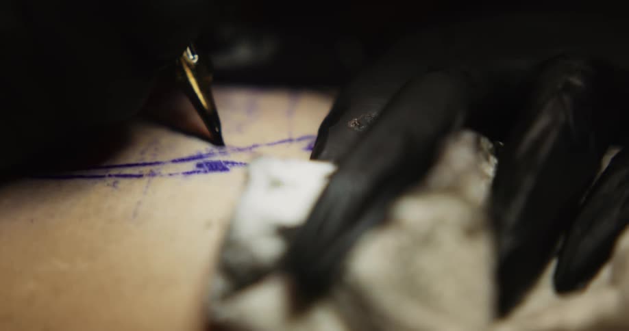 A tattoo artist outlines a design on a clients skin