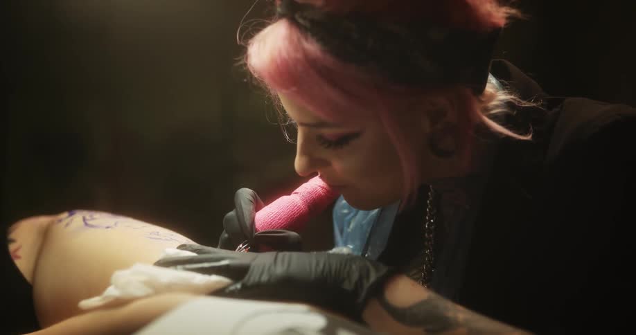 A tattoo artist looks at a drawing as she tattoos a womans thigh