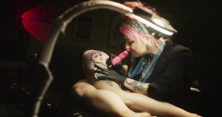 Happy tattoo artist with colorful hair tattooing on the leg of a customer
