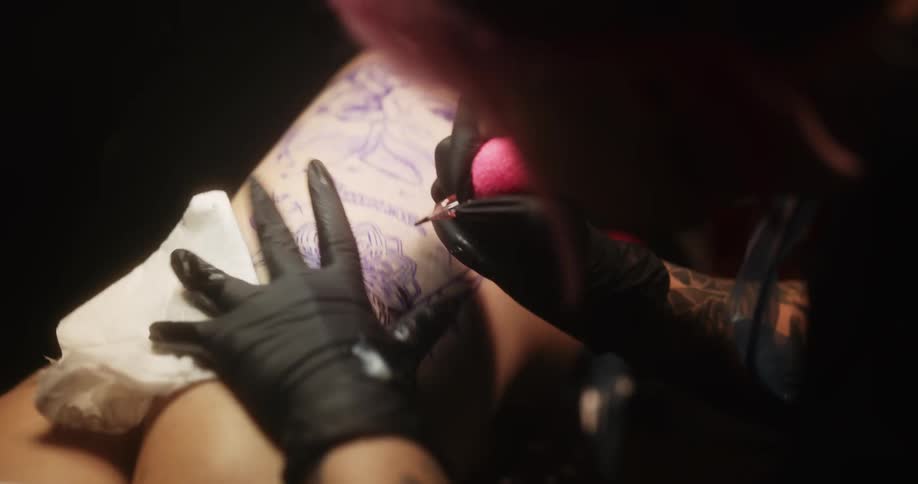 Close up of an artists using a tattoo machine on the skin of a customer