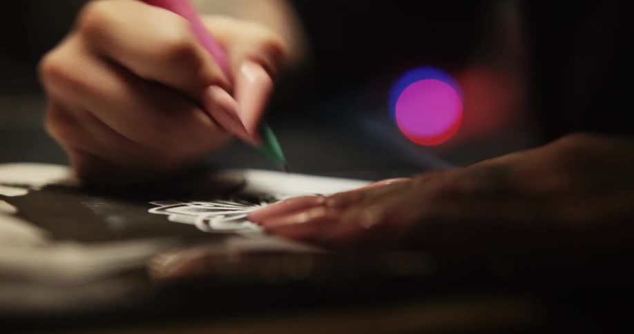 A person with pink fingernails traces a design with a pen