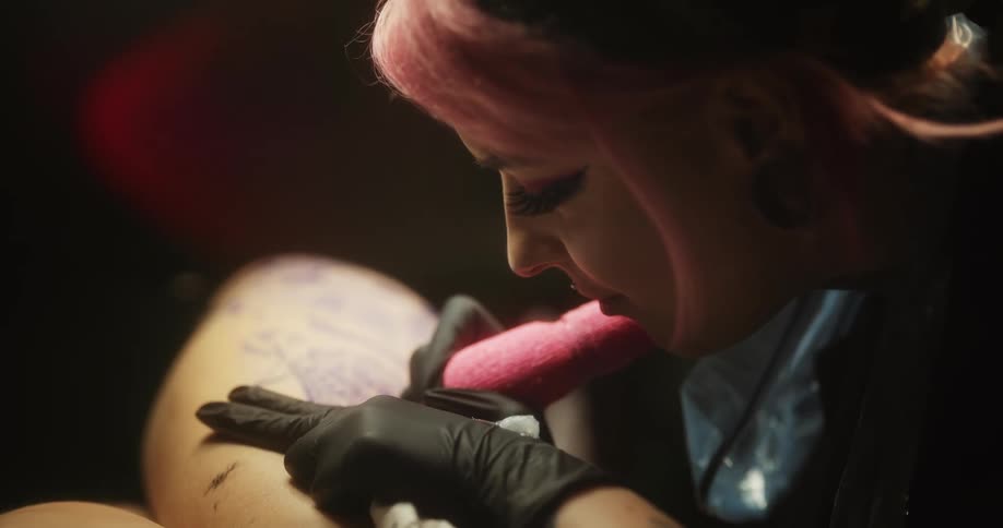 Close up of a tattoo artist with colorful hair working on the skin of a client