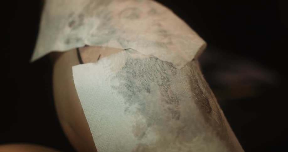 Close up of a tattoo artist covering the skin of a client after a session with wet paper towels