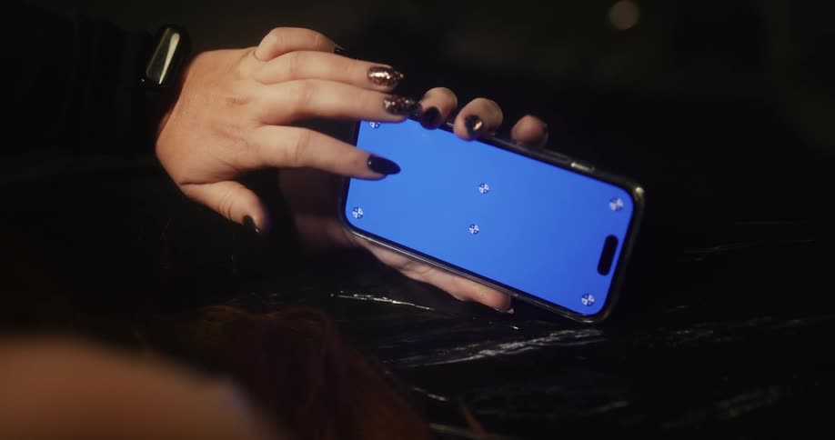 A woman with long dark painted fingernails is holding a cell phone in her hand and moving her finger across the blue screen