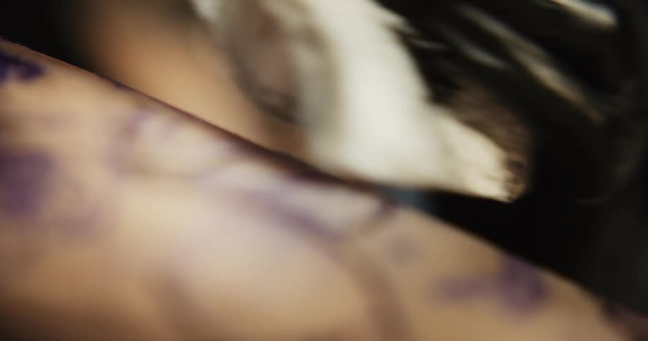 A tattoo artist tattoos on a person and then wipes the ink with a cloth