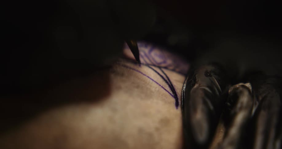 Close up of an artists using a tattoo machine on the skin of a customer