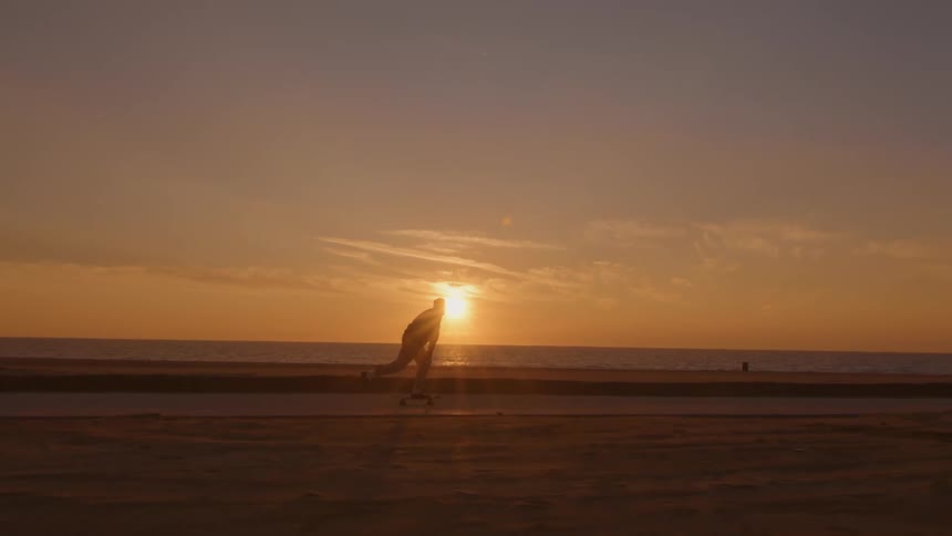 A silhouetted man skateboarding along a beachfront at sunset