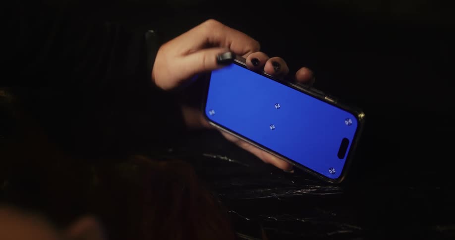 A woman with long dark painted fingernails is holding a cell phone in her hands with a blue screen