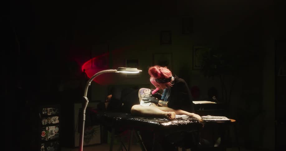 A woman is laying on a table with her legs exposed as another woman gives her a tattoo