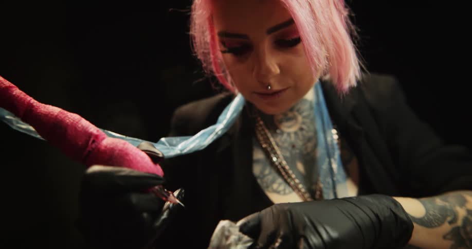 A female tattoo artist uses a tattoo gun to tattoo another person