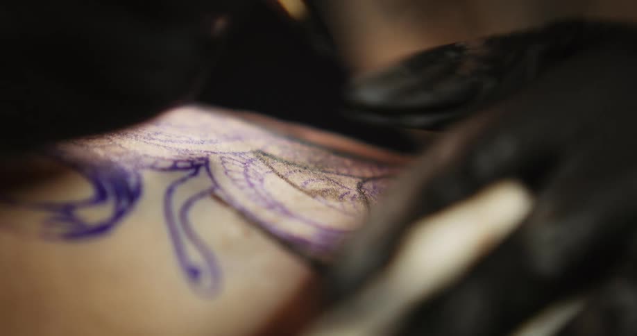 Tattoo artist applies ink to tattoo then wipes excess with a cloth
