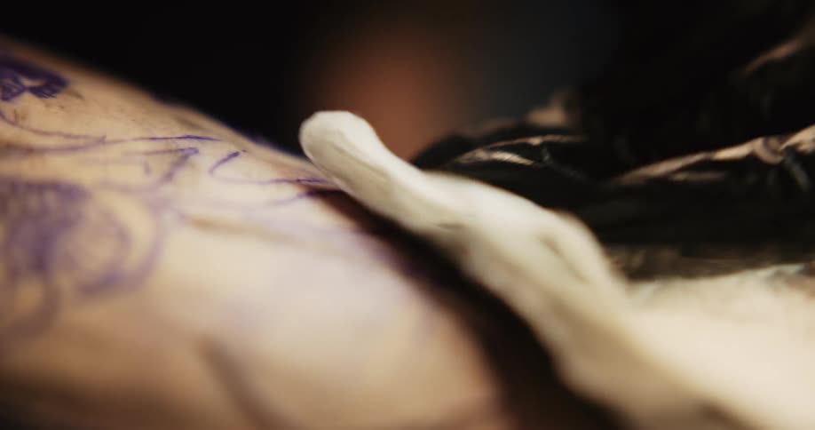 A tattoo artist applies ink to someone and then blots it with a cloth