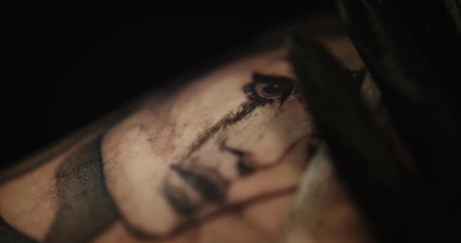 A person wearing a black glove wipes away excess ink as they give a tattoo