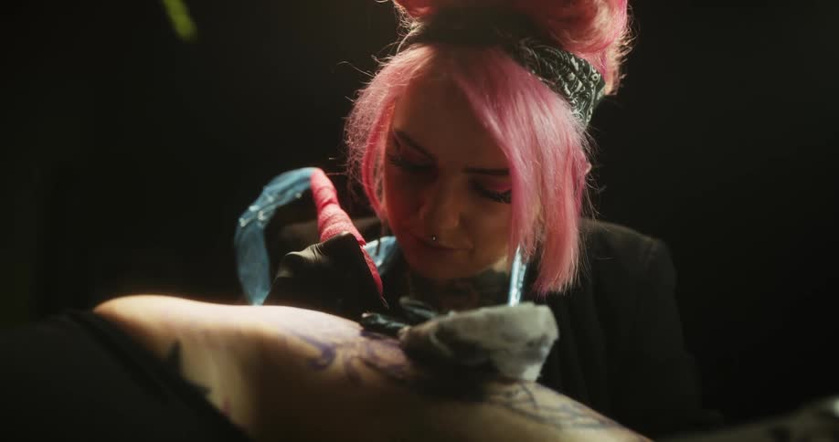 Close up of a tattoo artist with colorful hair working on the skin of a client