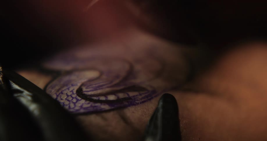 A tattoo artist working on a client while wearing black gloves