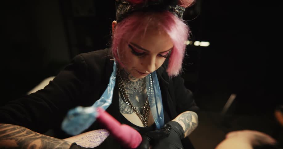 Close up of a tattoo artist with colorful hair working on the skin of a client