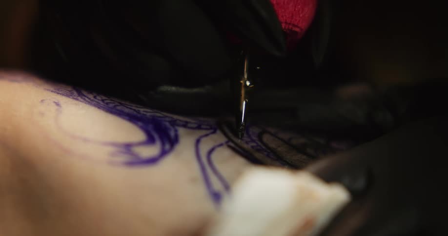 A tattoo artist applies in on a client and then wipes the skin with a cloth