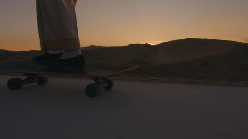 A man and another person are riding skateboards on a road along the coast with the sun setting in the distance