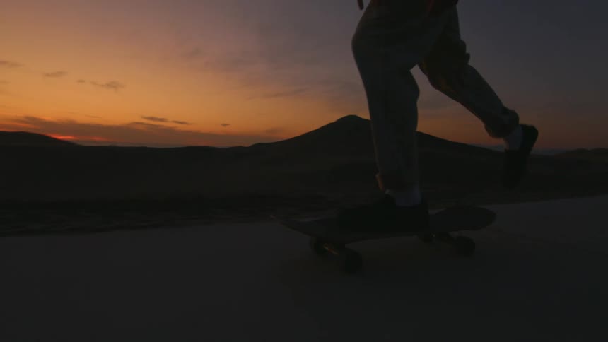 Skateboarder silhouetted against a red skyrides skateboard along sidewalk