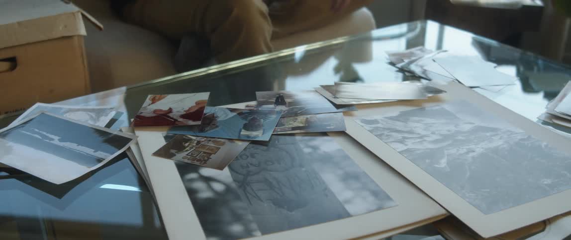 A man is stting down looking at photographs spread across a glass tabletop