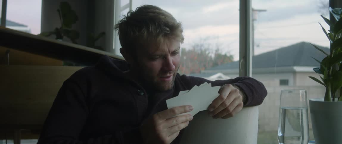 A man is sitting down smiling and talking to himself as he looks at a handful of photographs he is holding