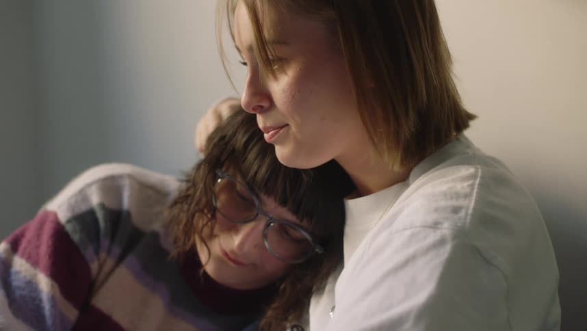 A female is stroking another females head who is sad and has her head on her shoulder
