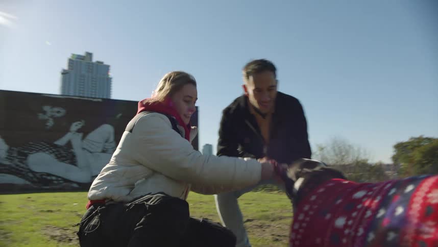 A man and woman are playing with a dog in a park in the city