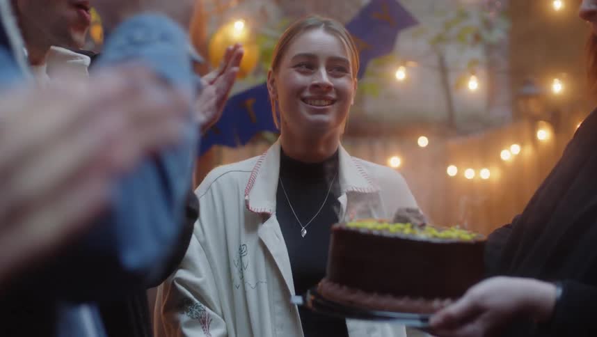 Young woman celebrating birthday with family and friends blowing out candles