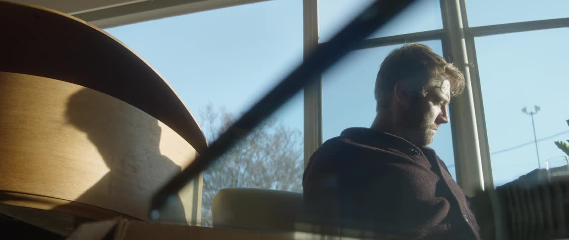 A man sitting in a room with a piano takes a sip of water from a glass