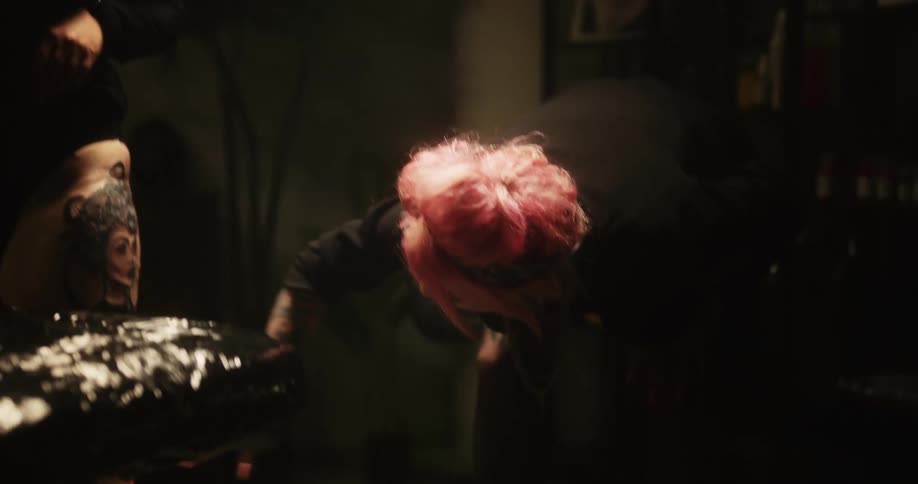 A tattoo artist with pink hair checking on a clients new tattoo