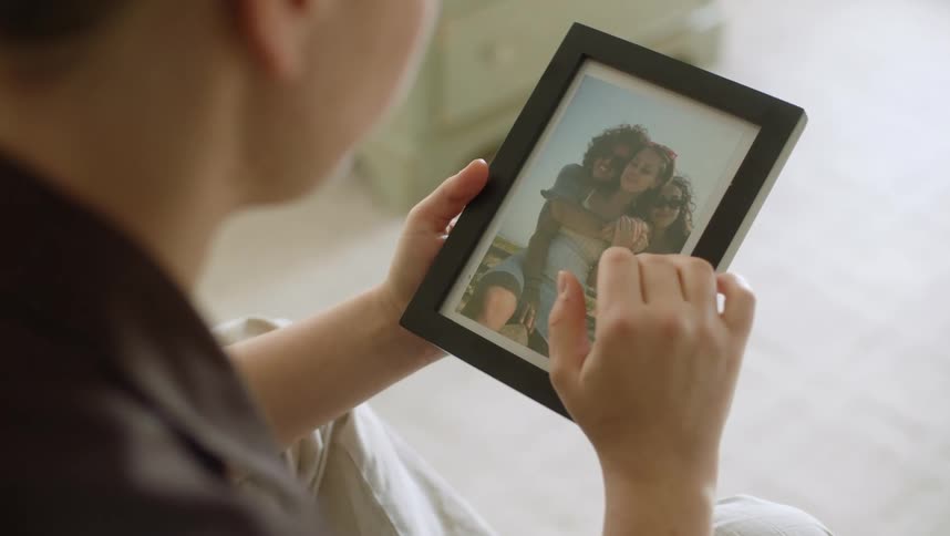 Person sitting at home gently touches a framed photograph of a group of women
