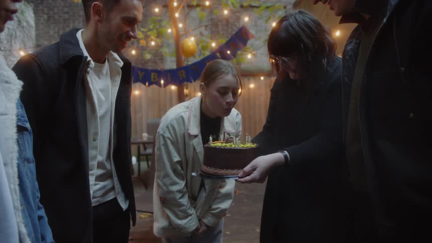 A group of people celebrate a woman blowing out candles on a cake