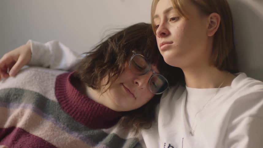 Two women sit together and one leans her head against the others shoulder