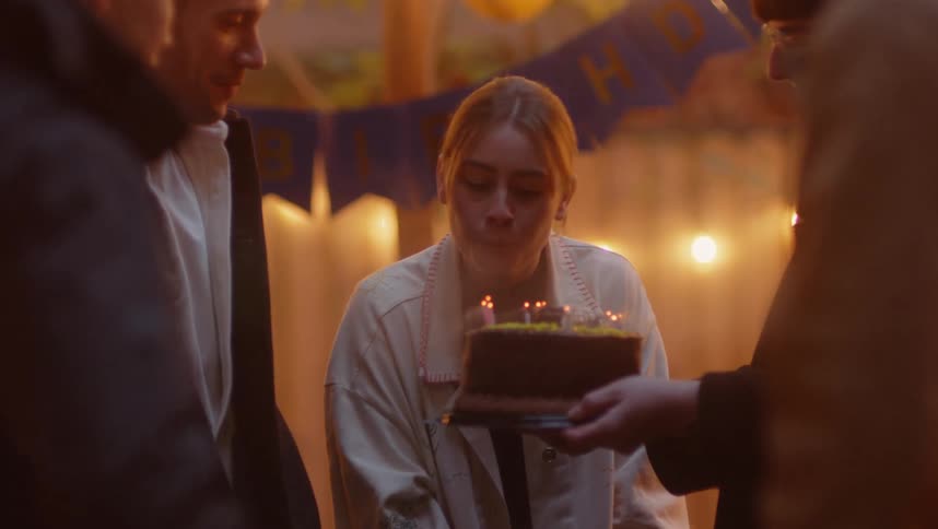 A young blonde woman blowing out birthday candles on a cake