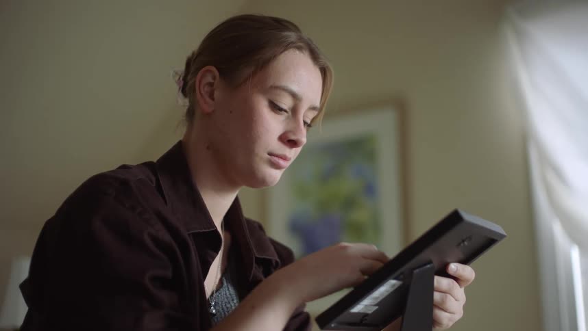 A woman holds and looks at a picture frame at home