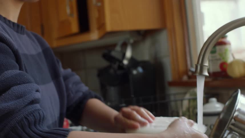 A woman washing a sink full of dirty dishes