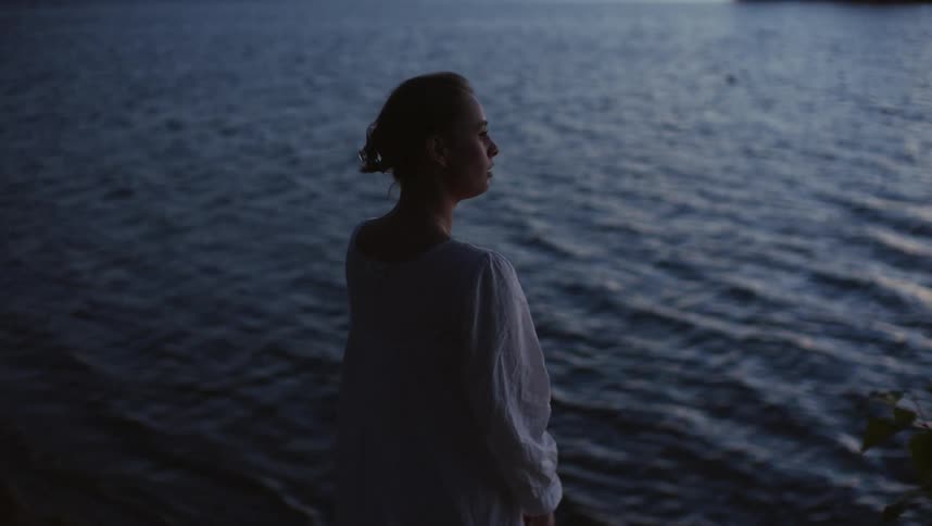 A woman stands next to the water and watches the waves