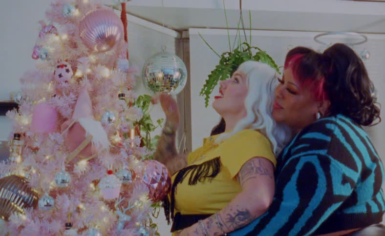 Two women embracing next to a pink christmas tree