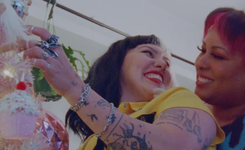 Two women are close and hugging as one fixes a doll