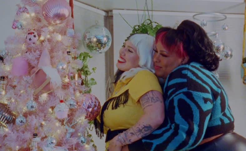 Young couple hug and kiss in front of a colorful pink christmas tree