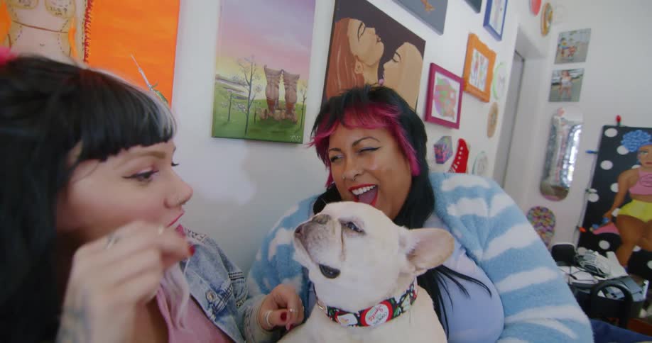 Two women are sitting on their living room couch playing with their pet bull dog