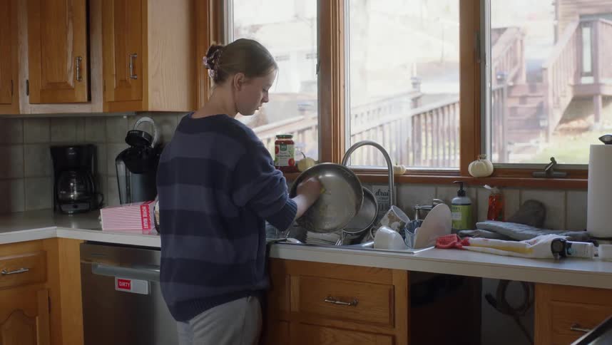Woman washes dishes while standing at sink with running faucet