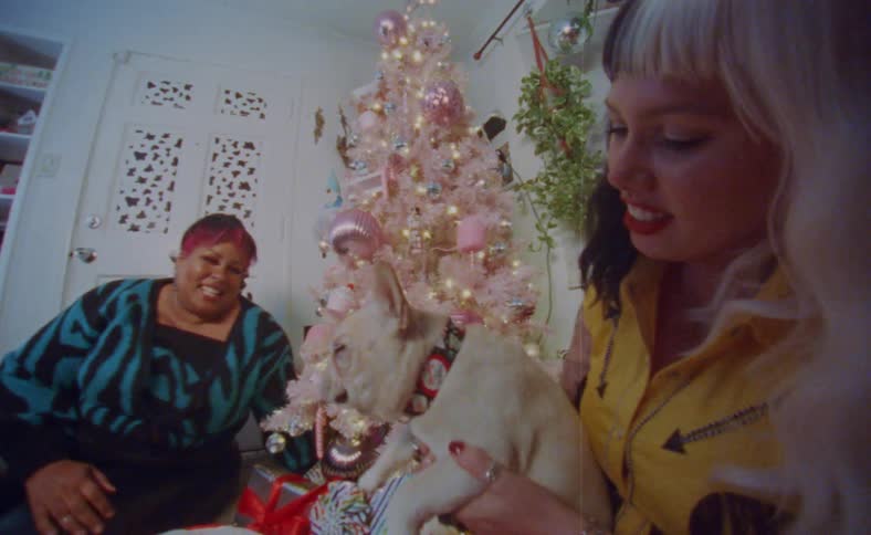 Two women sit near christmas tree kissing and cuddling dog