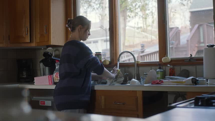 A woman is standing over the kitchen sink full of dishes waslking a large mug