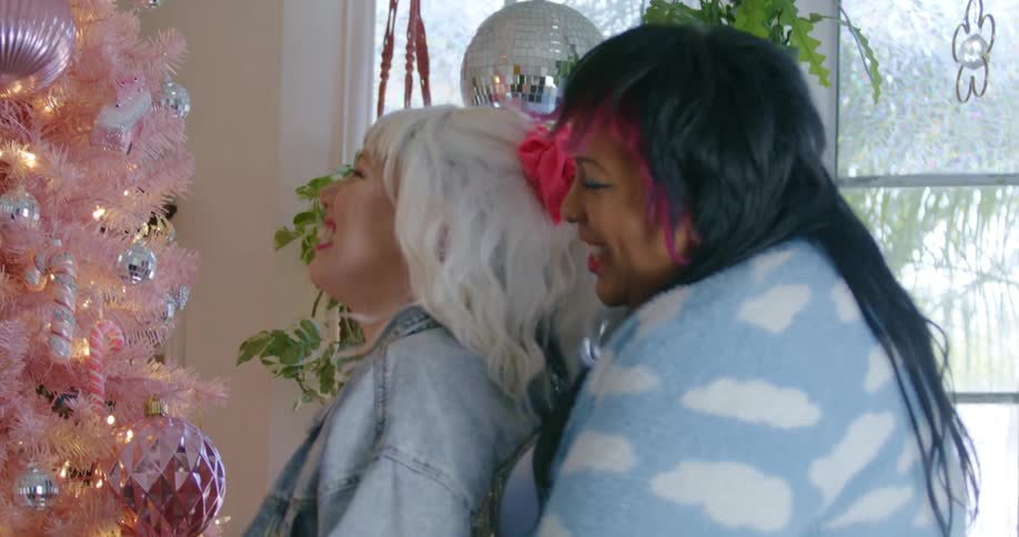 Young happy couple hug in front of a colorful pink christmas tree