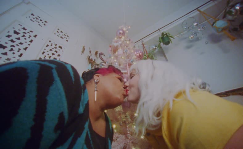 Young couple hug and kiss in front of a colorful pink christmas tree
