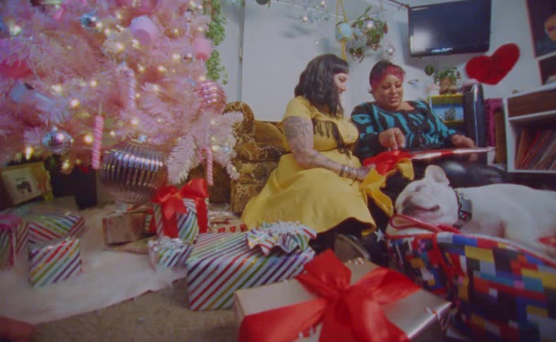 Women are sitting ona couch opening christmas gifts